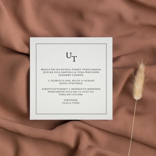 Neliönmuotoinen hääkutsu valkoisella taustalla, sijoitettuna lämpimän ruskealle kankaalle, kuivattu koristeheinä vieressä.