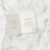 Taitettu A6-hääkutsu marmorialustalla – sisältä löytyy vihkiseremonian ja juhlan tiedot sekä toive lahjojen suhteen.