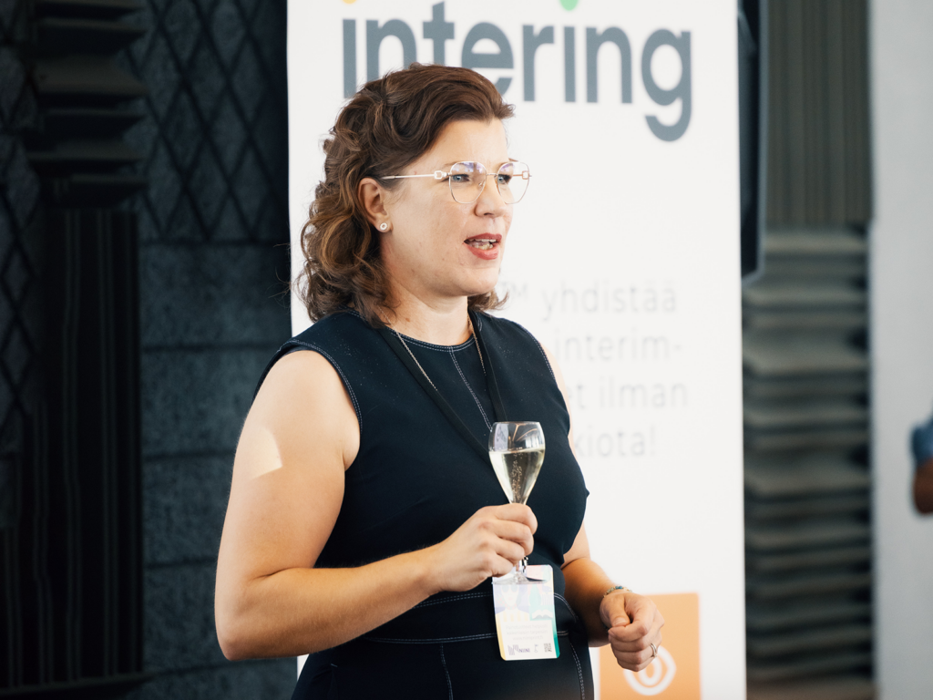 ainen pitää puheenvuoroa Intering-tapahtumassa, taustalla Intering-logo.