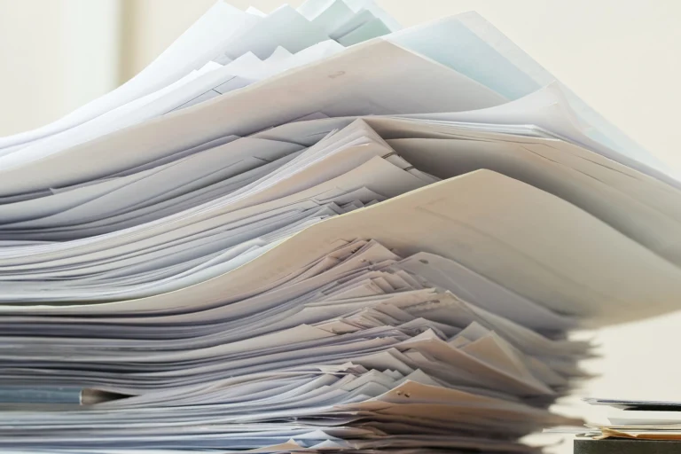 Suuri pino papereita ja asiakirjoja toimistopöydällä.