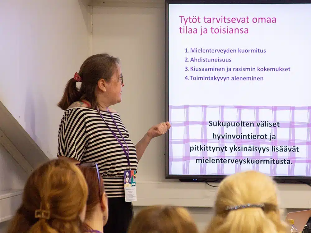 Puhuja esittelee tyttöjen hyvinvointiin liittyviä aiheita yleisölle valkokankaan vieressä.